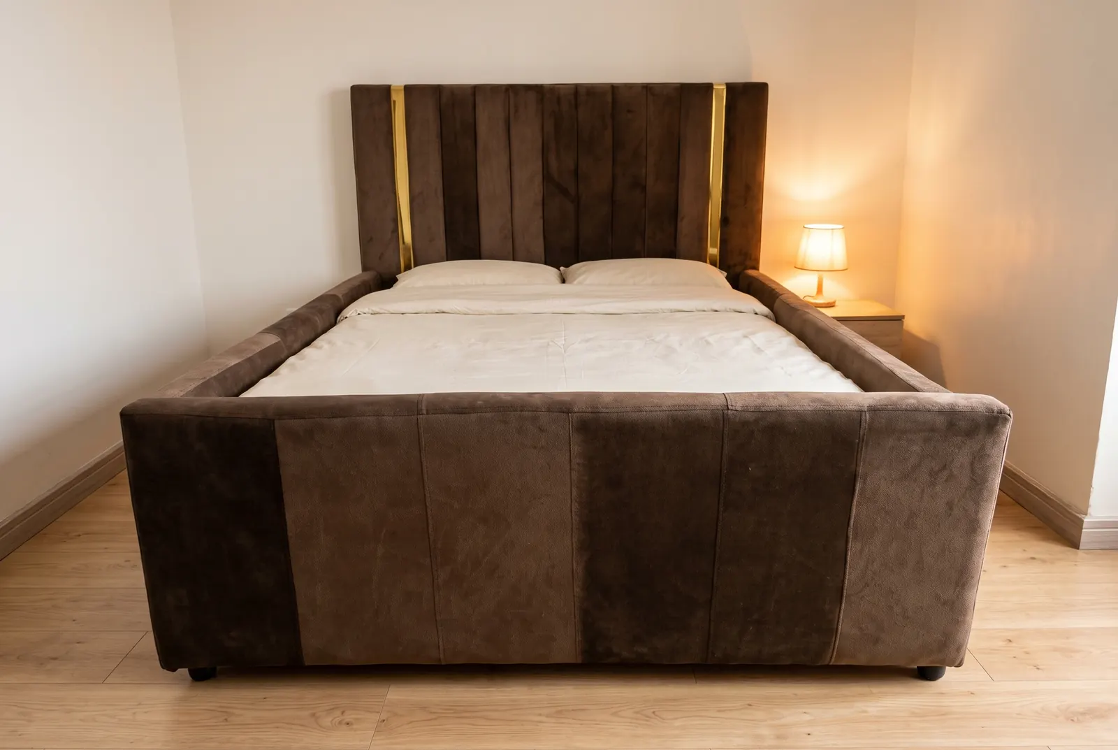 A brown suede bed with a banded headboard, brass trim, tall padded side rails and a high banded footboard, in a warm bedroom