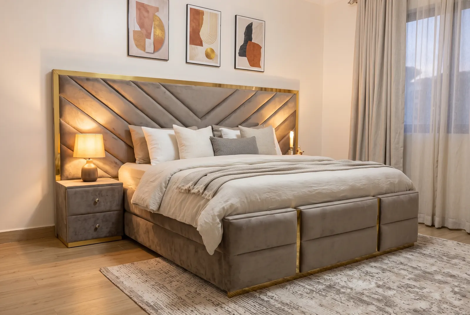 A taupe velvet bed with a chevron-panel headboard edged in gold, a matching bedside table and a gold-banded footboard