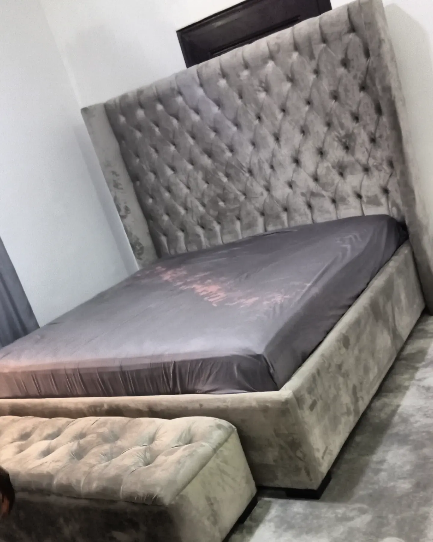 A tall grey velvet button-tufted bed with a matching tufted bench at its foot
