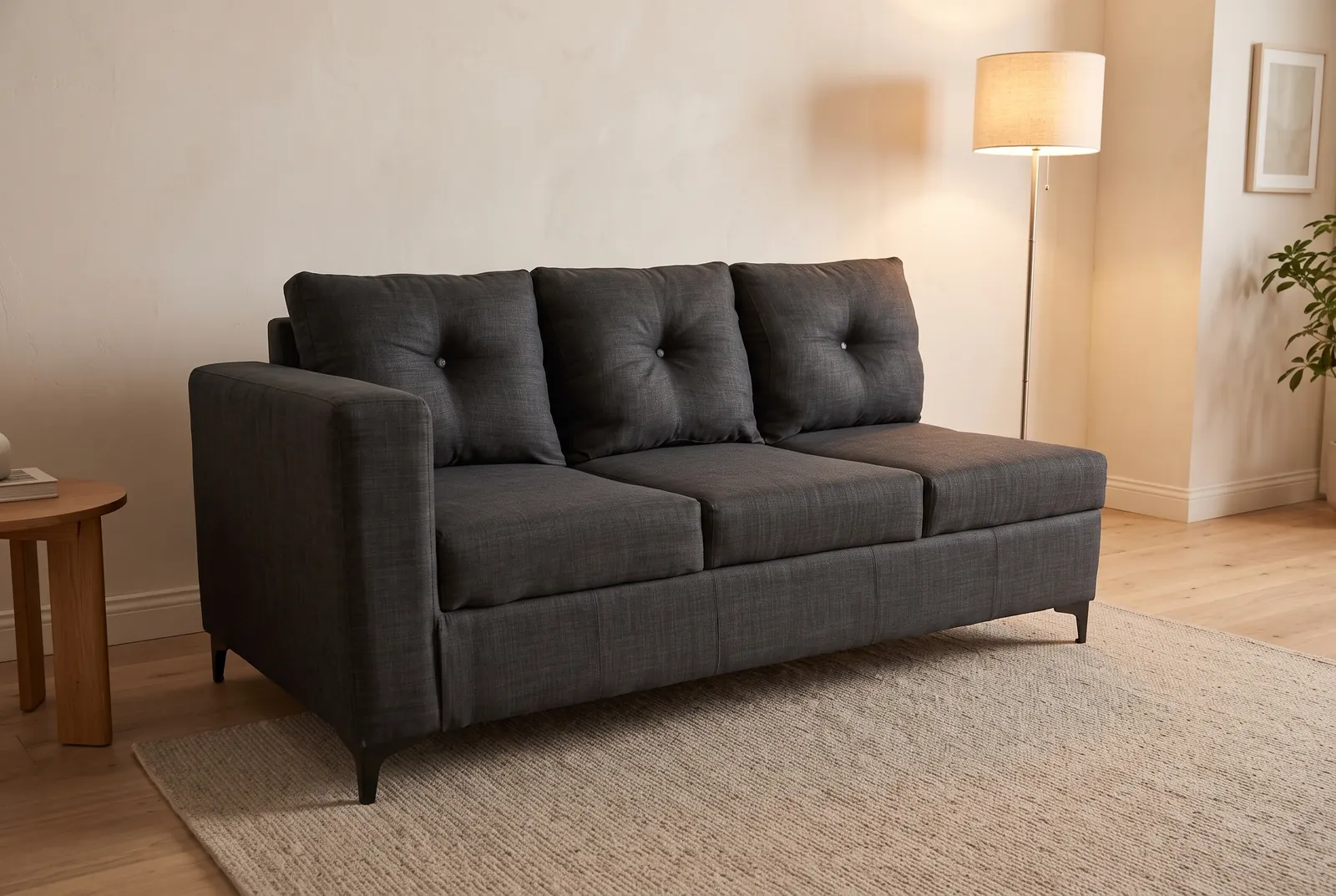 A charcoal three-seater sofa seen from the side, with a floor lamp and a round side table