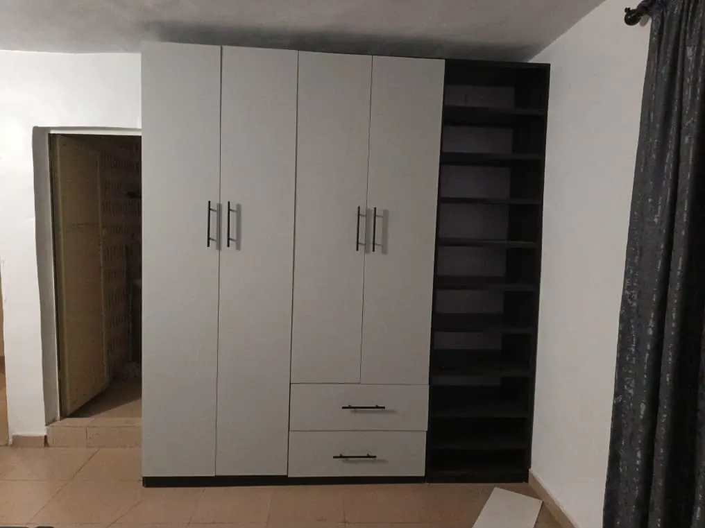 A finished fitted wardrobe with grey doors, two drawers and an open dark shelf tower beside a door